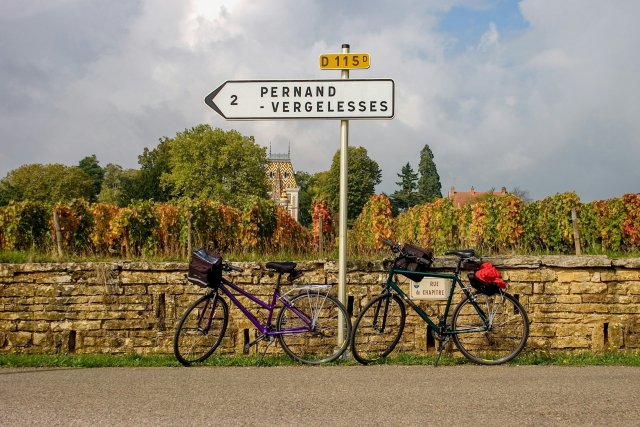 Two bikes leaning against a wall in front of a vineyard in Burgundy