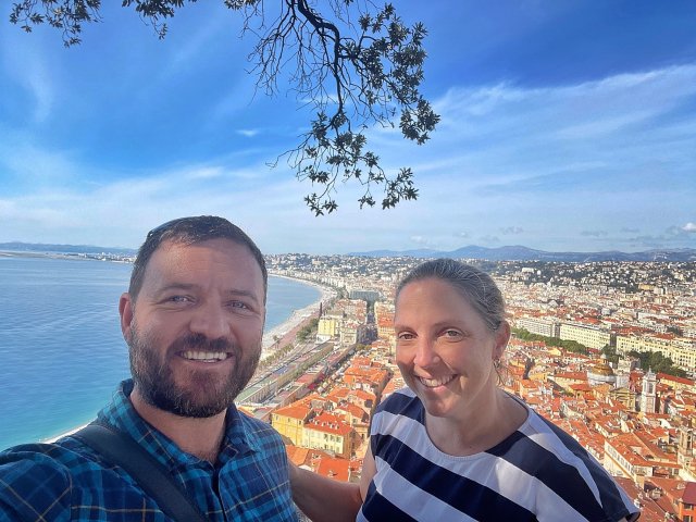 A smiling couple in the foreground with the city of Nice and the Mediterranean in the background