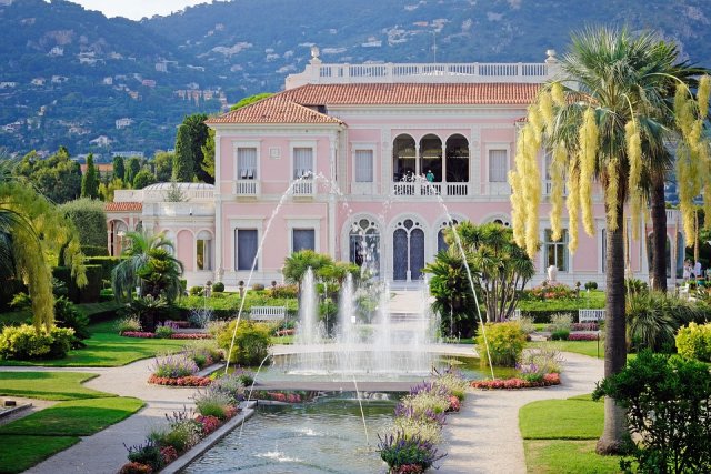 The pink and white Villa Ephrussi with manicured gardens and fountains in front